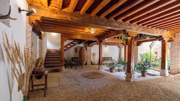 A rustic interior with a stone floor, wooden beams, a staircase, and potted plants.