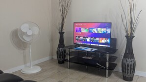 A living room with a flat-screen TV, a standing fan, two decorative vases, and a black leather sofa.