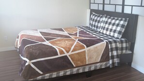 A bed with a geometric-patterned bedspread and a checkered pillow, a dark wooden floor, and a wall with a panel design.