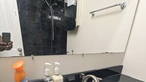 A bathroom with a black countertop, a white sink, a mirror, and a shower.