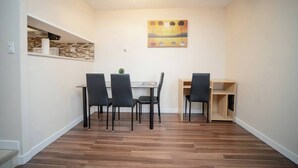 A dining area with a table and chairs, a wall-mounted shelf, and a ceiling light fixture.