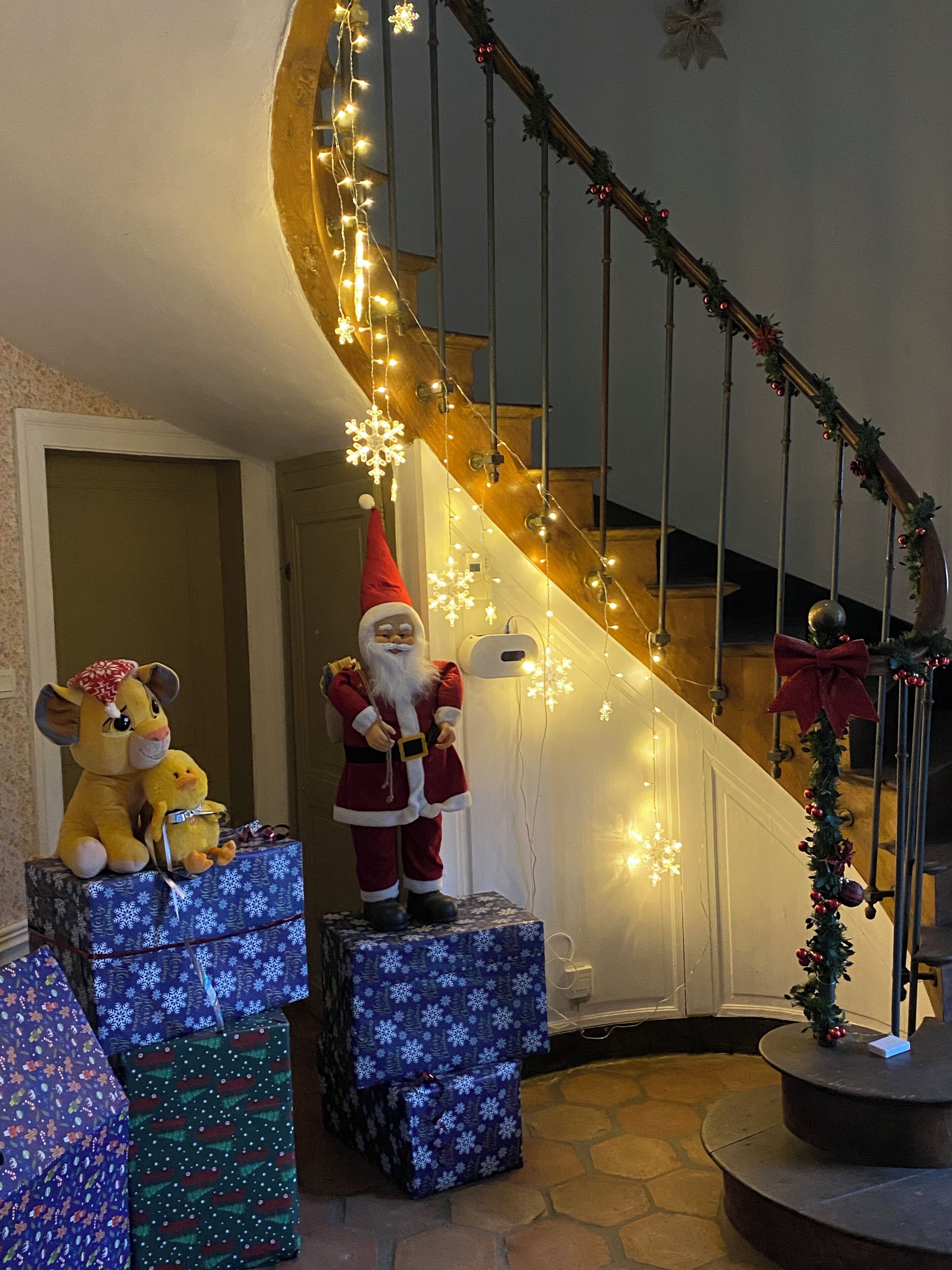 A staircase decorated with Christmas lights and garlands, with a Santa Claus figure and plush toys on the steps.