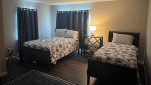 Ein Hotelzimmer mit zwei Einzelbetten, einem kleinen Tisch mit Lampe und einem Fenster mit Vorhängen.