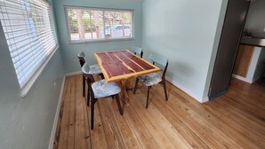 A dining area with a wooden table and four chairs, a ceiling fan, and a window with blinds.