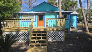 A small, single-story house with a blue exterior and a wooden deck.