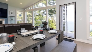 Un'elegante sala da pranzo con un tavolo lungo apparecchiato per quattro persone, un'accogliente zona salotto con divano e ampie finestre con vista sull'esterno.