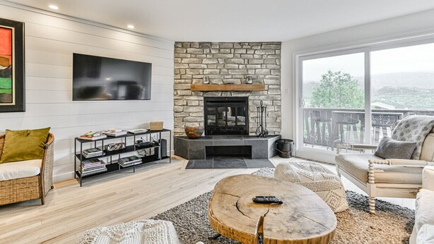 Un salon moderne doté d’une cheminée en pierre, d’un téléviseur à écran plat, d’une bibliothèque et d’un balcon aménagé avec du mobilier d’extérieur.