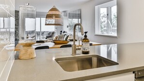 Une cuisine moderne avec un évier en acier inoxydable, un saladier en bois, un bocal en verre et un luminaire suspendu.