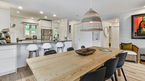 Une cuisine moderne avec des meubles blancs, une table à manger en bois et un luminaire suspendu.