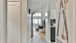 A modern interior with a hallway leading to a living area, a kitchen with a dining table, and a large window providing natural light.