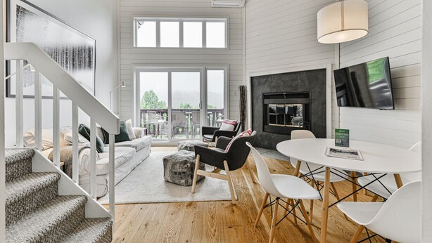 A spacious living area with a fireplace, a dining table, and a staircase leading to another level.