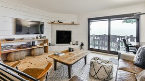 A modern living room with a fireplace, a large TV, and a view of the outdoors.