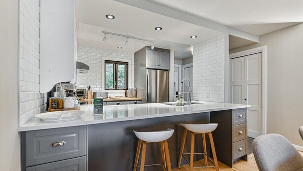 A modern kitchen with a large island, grey cabinetry, and wooden stools.
