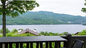 A deck with a table and two wicker chairs overlooking a lake with a mountain in the background.