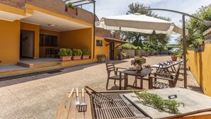 Un patio al aire libre con mobiliario de madera, una parrilla y plantas en macetas.