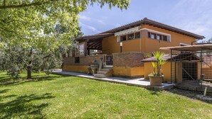 Una casa de dos pisos con un patio, una zona de estar cubierta al aire libre y un muro de ladrillo.
