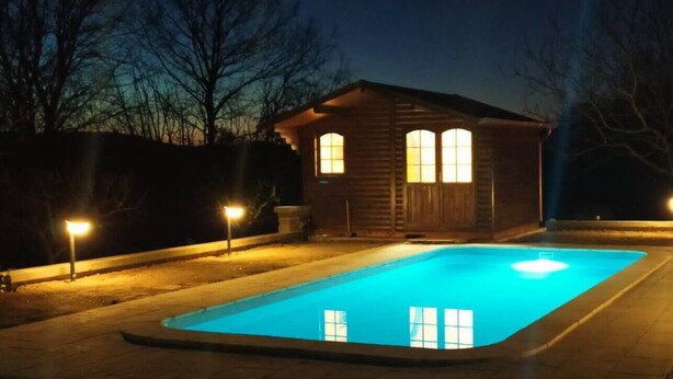 Una cabaña de madera con piscina, iluminada por farolas durante la noche.