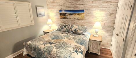 Quarto com cama, duas mesas de cabeceira com luminárias, painel de parede de madeira, um quadro e uma porta.