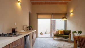 Une cuisine compacte équipée d’une cuisinière intégrée, d’un évier et d’un réfrigérateur. On y trouve également un coin repas avec une table en bois et un canapé vert.