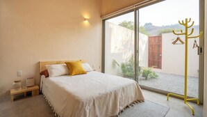 A bedroom with a bed, bedside table, and a window with a view of the outdoors. - Casa Oma 04: in the heart of Tepoztlán (Tepoztlán)