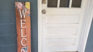 Una puerta blanca con un ventanal, un cartel de bienvenida y un timbre.