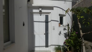 A white door with a small window above it, a security camera, and a potted plant beside the door. - AMZ Apartments (Kato Gouves)