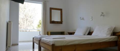 A bedroom with a wooden bed, a flat-screen TV mounted on the wall, an air conditioning unit, and a window with curtains.