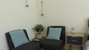 A modern room with two black sofas, a small table with a plant, a bedside table with a lamp, and a wall socket. - AMZ Apartments (Kato Gouves)
