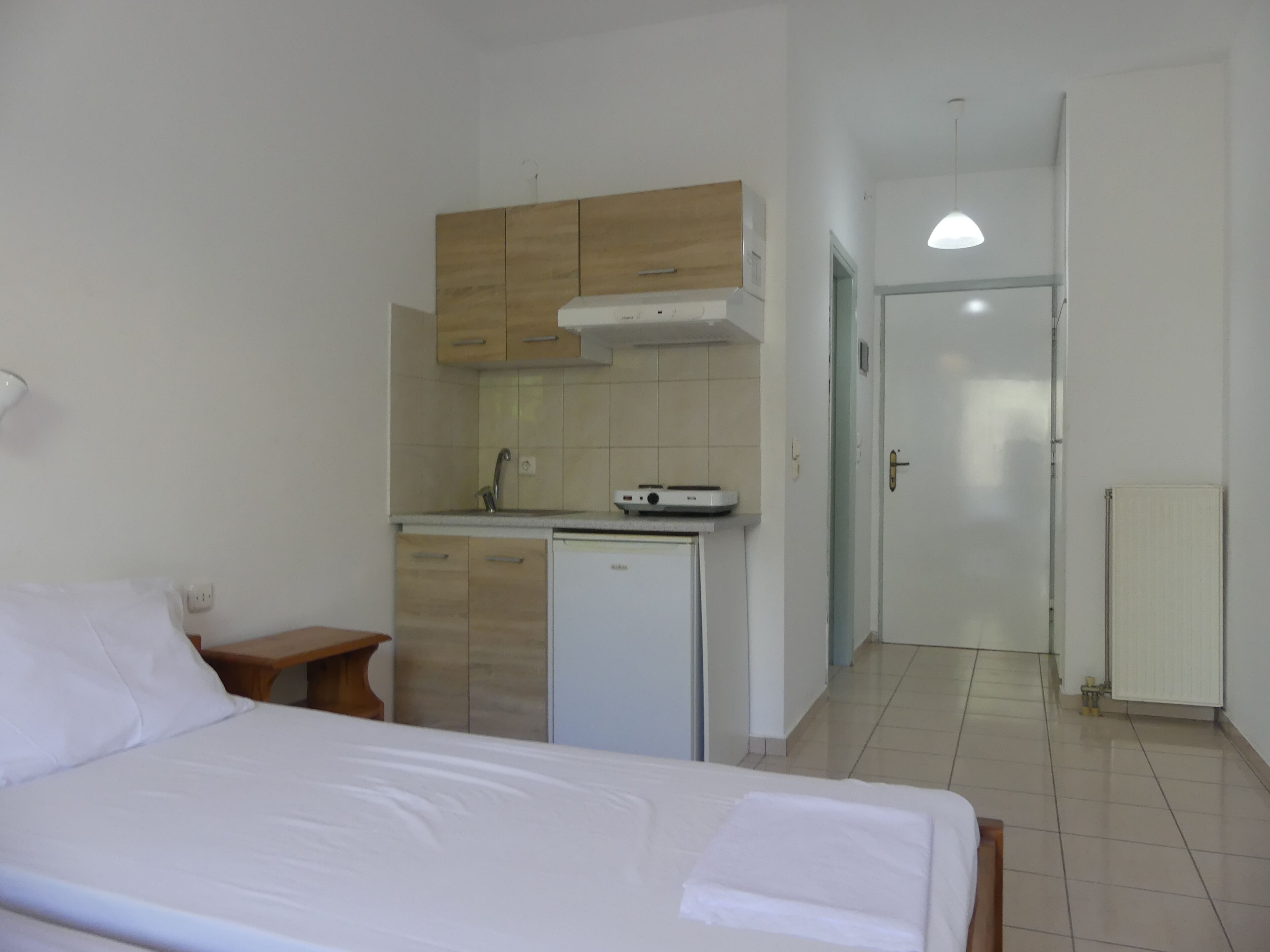 Une chambre d’hôtel de taille réduite, comprenant un lit, une petite kitchenette et une porte donnant sur une autre pièce.