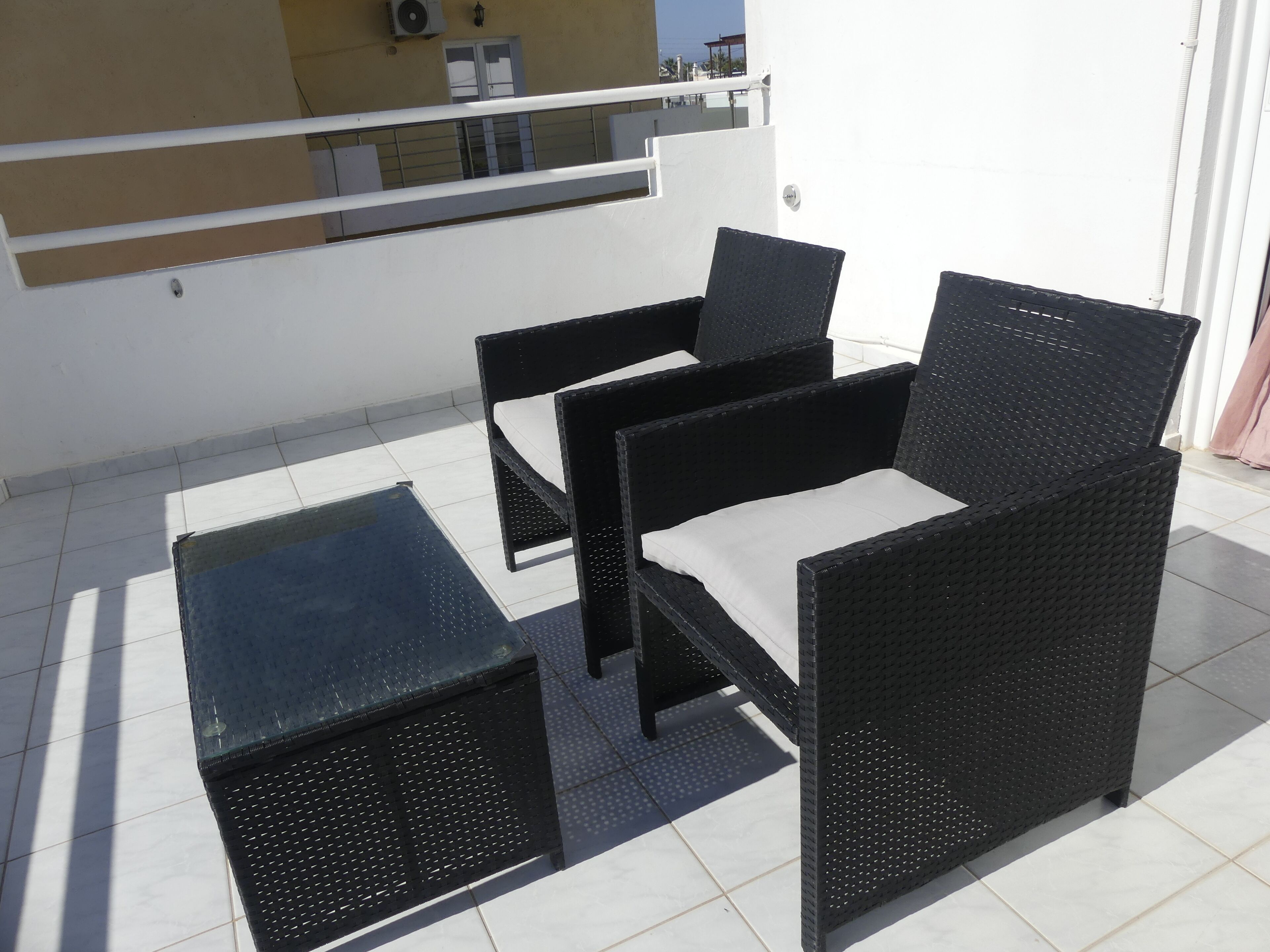 Un patio con un conjunto de sofá y sillón de ratán negro, y una mesita.
