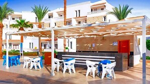 Un espace extérieur aménagé avec des chaises en plastique blanches et bleues, une porte rouge et un patio couvert doté d’une pergola.