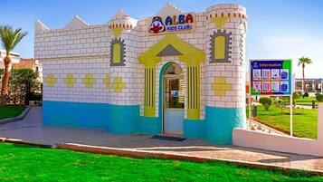 A children's club building with a castle-like facade, a signboard, and a grassy area in front.