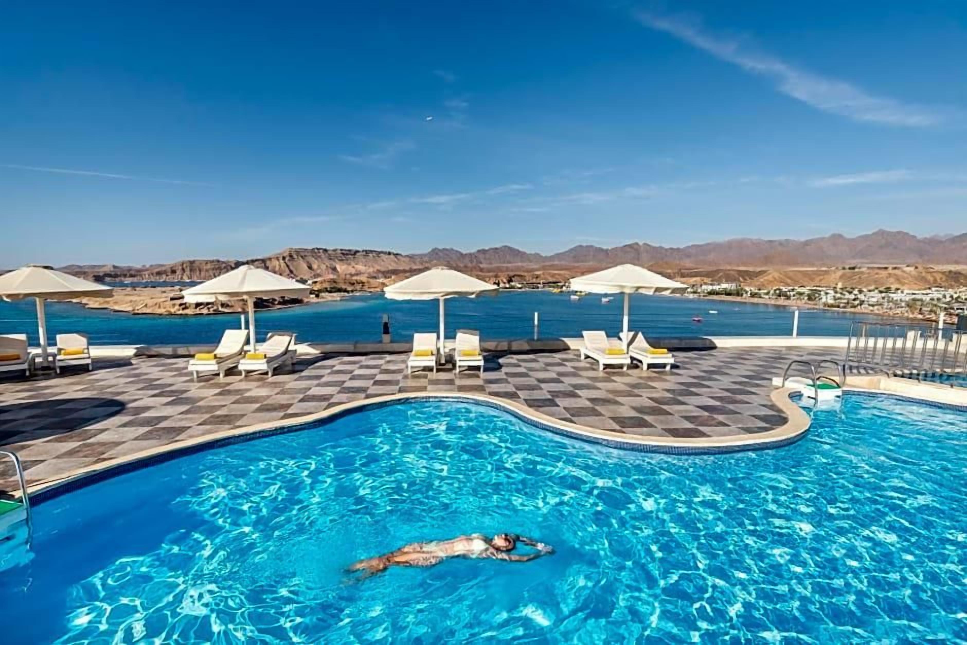 Une piscine entourée de montagnes, avec des chaises longues et des parasols.