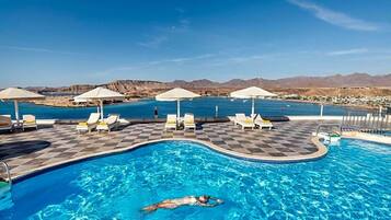 Une piscine entourée de montagnes, avec des chaises longues et des parasols.
