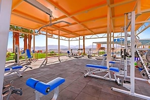 Une salle de sport en plein air équipée de divers appareils d’exercice, notamment des bancs et des machines de musculation, située sous un espace abrité offrant une vue sur les montagnes.