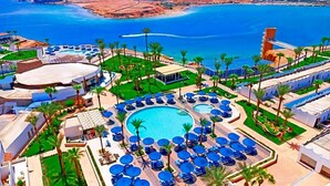 Ein Resort mit einem zentralen Schwimmbecken, umgeben von Liegebereichen mit Sonnenschirmen, Palmen und Meerblick.