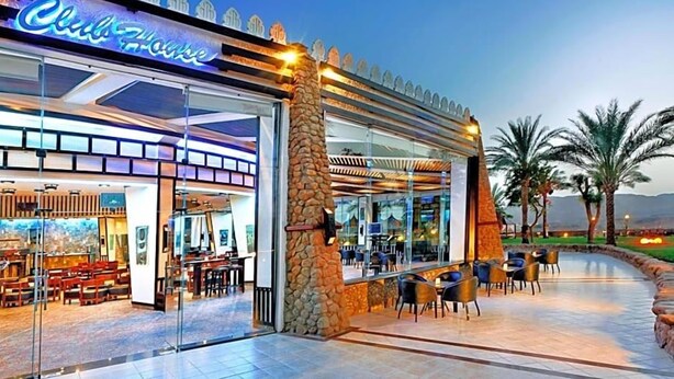 Un restaurant doté d’une façade en verre, de places assises en plein air et d’un pilier en pierre.