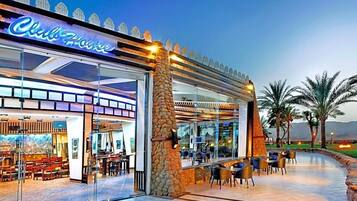 Un restaurant doté d’une façade en verre, de places assises en plein air et d’un pilier en pierre.
