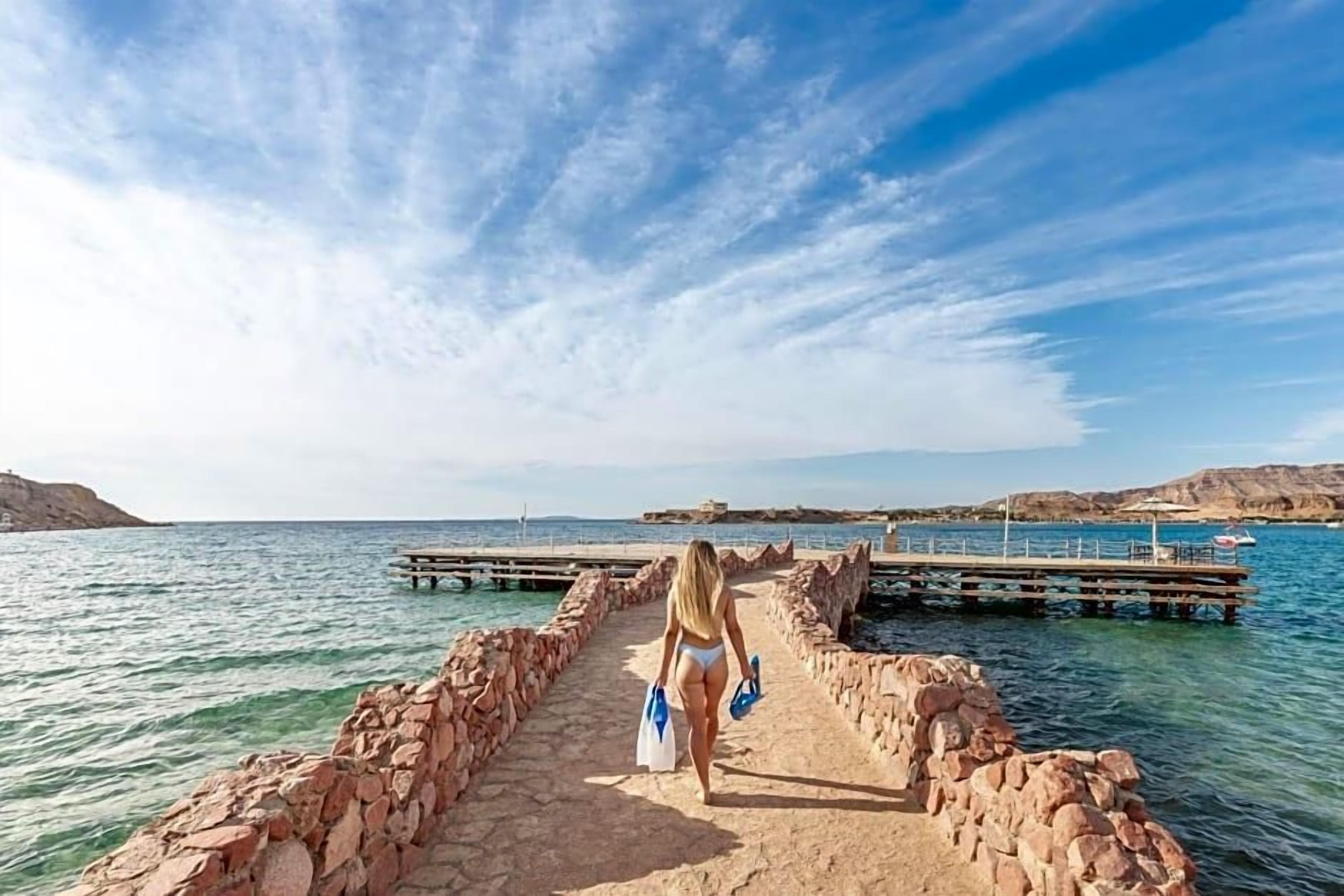 Un camino de piedra que lleva a un muelle sobre aguas tranquilas, con un cielo despejado.