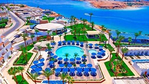 A resort with a central swimming pool surrounded by sun loungers and palm trees, a road curving around the property, and a beach in the background. - Albatros Sharm Resort By Pickalbatros (Sharm El Sheikh)