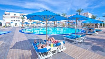 A poolside area with lounge chairs and umbrellas, a pool, and buildings in the background.