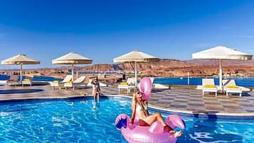 A pool area with lounge chairs and umbrellas, a pool, and a mountainous backdrop.