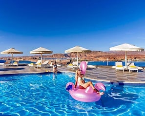 Un espace piscine avec des chaises longues et des parasols, une piscine et un paysage montagneux en arrière-plan.