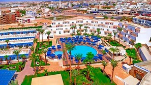Ein Resort mit einem zentralen Schwimmbad, umgeben von Liegebereichen und Palmen.