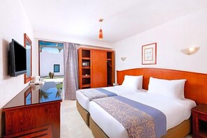 Een hotelkamer met twee bedden, een televisie, een houten bureau en een kledingkast.
