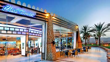 A restaurant with a stone facade, outdoor seating, and a view of palm trees.