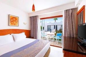 A hotel room with a bed, a television, and a balcony with chairs and a table.