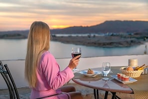 Eine Person sitzt an einem Tisch mit einem Glas Rotwein, einer Speiseplatte und einem Brotkorb.