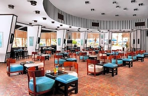 Eine Hotelhalle mit mehreren Sitzbereichen, darunter Tische und Stühle, sowie einem gemusterten Boden.