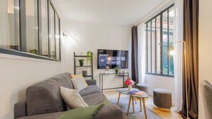 A modern living room with a grey sofa, a small coffee table, and a flat-screen TV mounted on the wall. - Beautiful Apartment at Gare de L'est Republique (Paris)